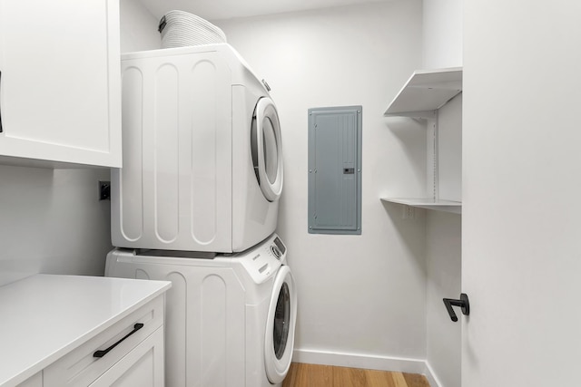 laundry area with baseboards, light wood finished floors, electric panel, stacked washer / drying machine, and cabinet space