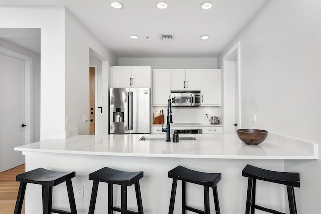 kitchen with a peninsula, stainless steel appliances, a breakfast bar, visible vents, and white cabinets