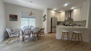 203 Evergrene Pkwy, Palm Beach Gardens, FL 33410 - kitchen with wall chimney exhaust hood, freestanding refrigerator, a peninsula, decorative backsplash, and light wood-style flooring