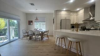 203 Evergrene Pkwy, Palm Beach Gardens, FL 33410 - kitchen with freestanding refrigerator, wall chimney exhaust hood, a peninsula, a breakfast bar area, and backsplash