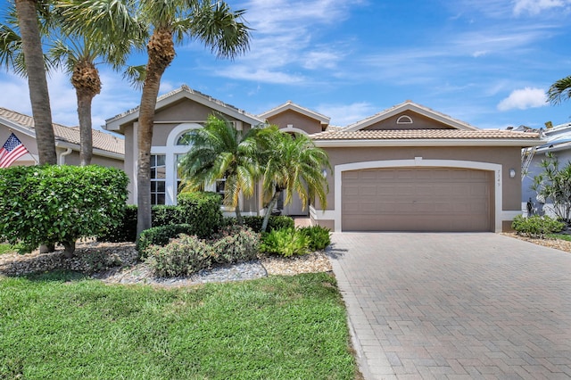 mediterranean / spanish house featuring stucco siding, a garage, decorative driveway, and a tiled roof