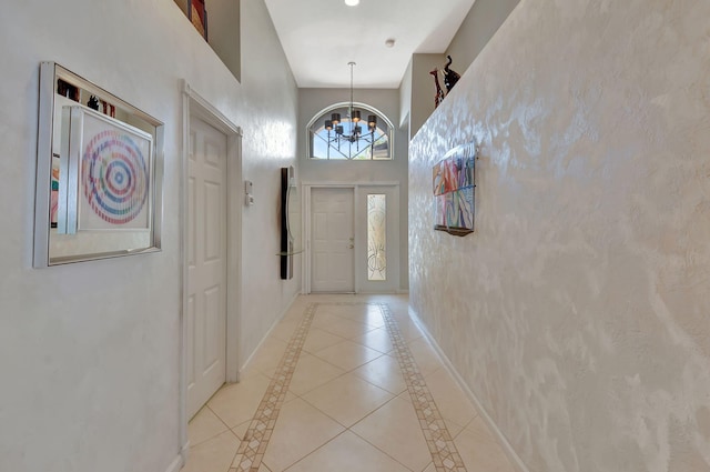 doorway featuring a chandelier, baseboards, light tile patterned flooring, and a towering ceiling