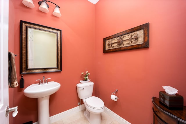 half bathroom with baseboards, toilet, tile patterned floors, and a sink