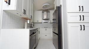 387 Enfield St, Boca Raton, FL 33487 - kitchen featuring wall chimney exhaust hood, freestanding refrigerator, light countertops, white cabinets, and decorative backsplash