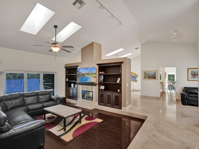 living area featuring track lighting, a skylight, a premium fireplace, a ceiling fan, and high vaulted ceiling