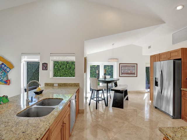 kitchen with stainless steel appliances, a sink, vaulted ceiling, brown cabinets, and light stone countertops