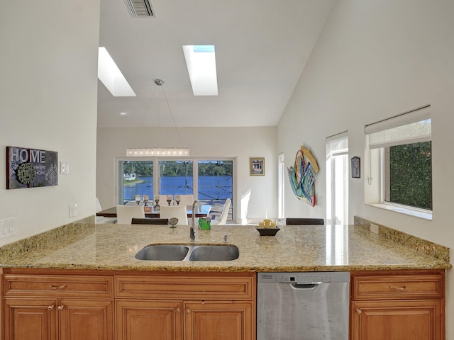 kitchen featuring stainless steel dishwasher, a sink, a skylight, light stone counters, and brown cabinets