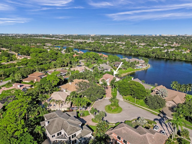 aerial view of property and surrounding area featuring a nearby body of water, nearby suburban area, and a tree filled landscape