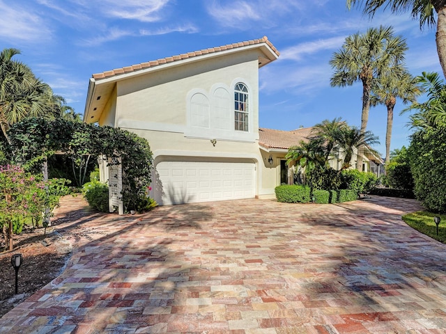 mediterranean / spanish house featuring a tiled roof, a garage, stucco siding, and driveway