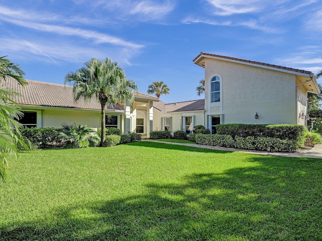 back of property with stucco siding, a yard, and a tile roof