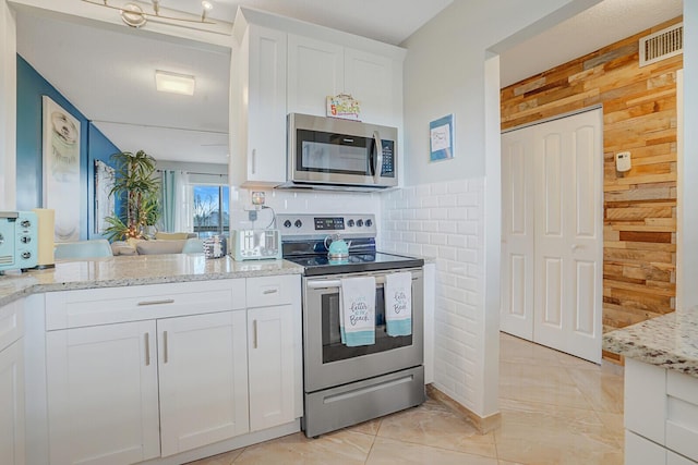 2724 N Garden Dr Unit 302, Lake Worth, FL 33461 - kitchen with appliances with stainless steel finishes, wooden walls, white cabinetry, light stone counters, and backsplash