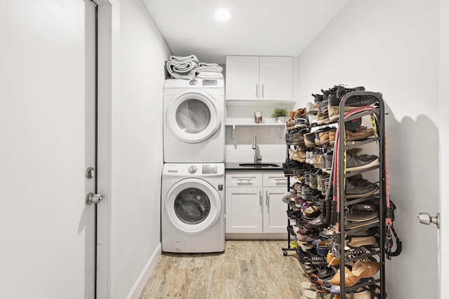 laundry room with cabinet space, stacked washer / dryer, light wood finished floors, and baseboards