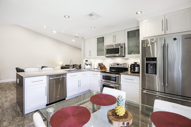 kitchen featuring appliances with stainless steel finishes, a sink, a peninsula, tasteful backsplash, and glass insert cabinets