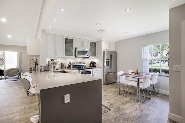 kitchen with appliances with stainless steel finishes, a sink, light wood finished floors, a peninsula, and a breakfast bar area
