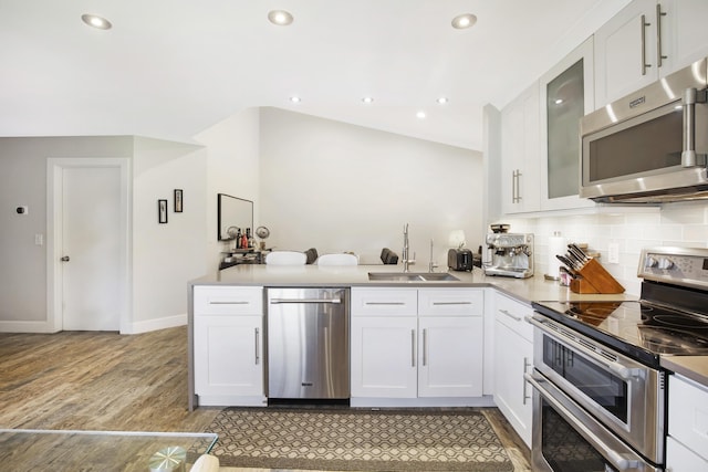 kitchen featuring appliances with stainless steel finishes, a sink, light wood-type flooring, decorative backsplash, and white cabinets