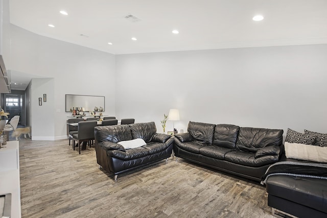 living room featuring wood finished floors, ornamental molding, baseboards, recessed lighting, and a high ceiling