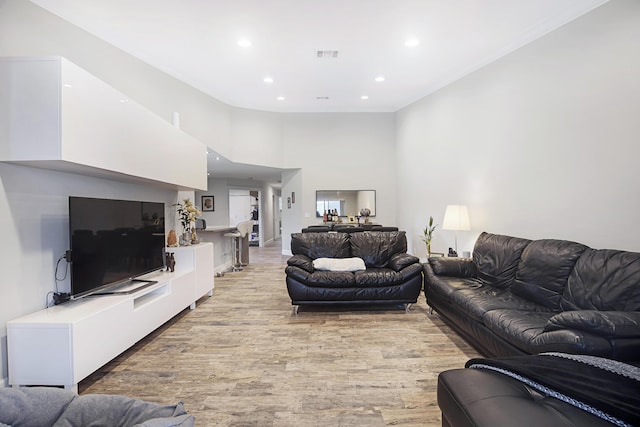 living room featuring light wood-type flooring, recessed lighting, crown molding, and a high ceiling