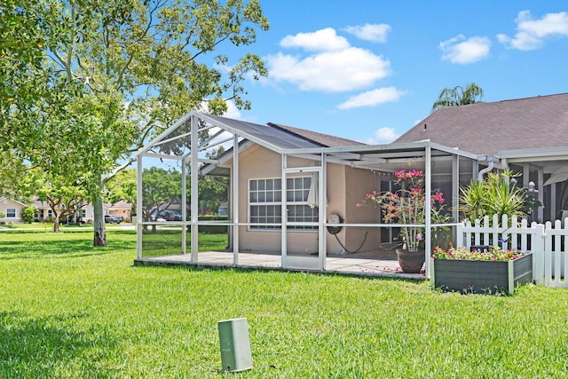 rear view of house featuring a patio, stucco siding, a yard, glass enclosure, and a shingled roof