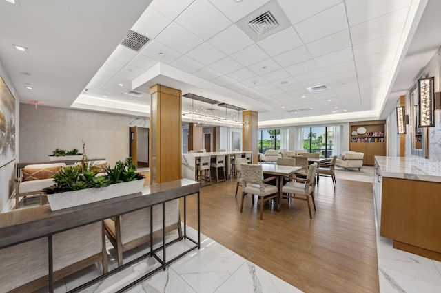 dining area with a raised ceiling, a drop ceiling, decorative columns, and light marble finish flooring