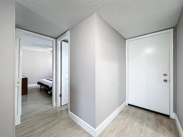 corridor featuring a textured ceiling, light wood-style flooring, and baseboards