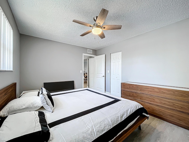 bedroom with a textured ceiling, wood finished floors, ceiling fan, and a closet