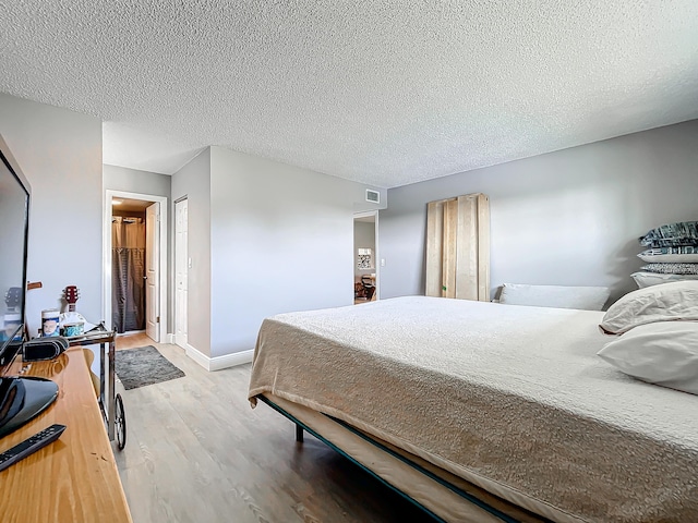 bedroom with light wood-style floors, a textured ceiling, and baseboards