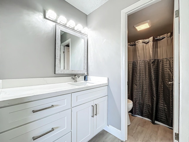 bathroom with wood finished floors, toilet, vanity, and a textured ceiling
