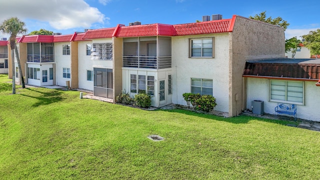 rear view of house with stucco siding, central AC unit, a yard, and a tile roof