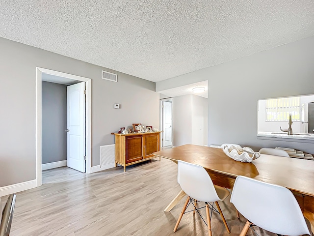 dining room featuring a textured ceiling, light wood-type flooring, and baseboards