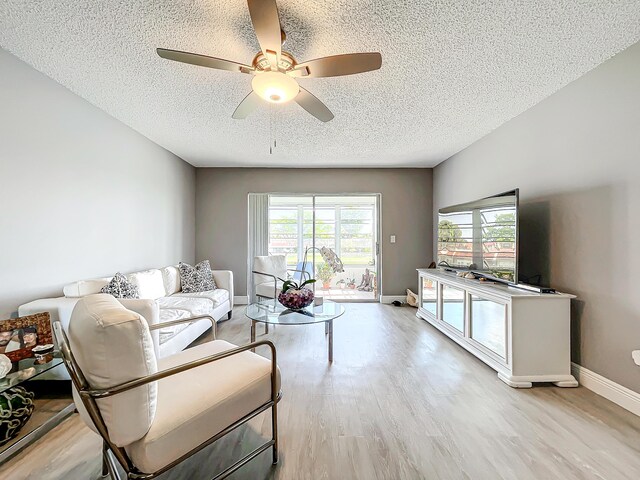 living room with a textured ceiling, ceiling fan, wood finished floors, and baseboards