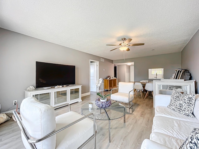 living area featuring a textured ceiling, light wood-type flooring, and ceiling fan