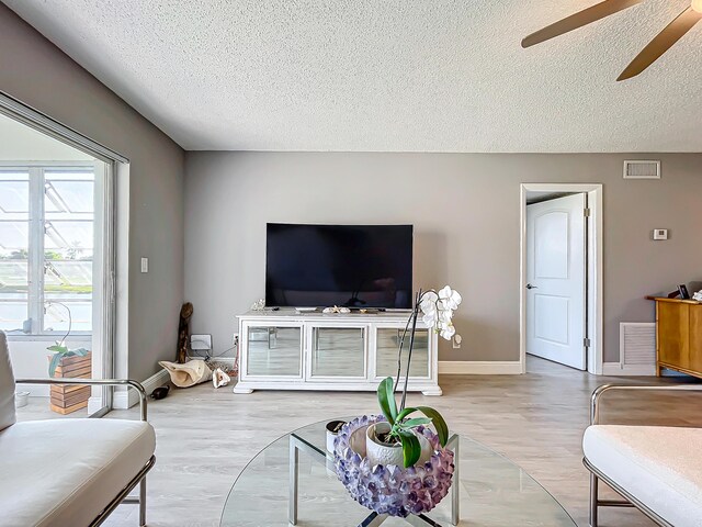 living room featuring a textured ceiling, ceiling fan, wood finished floors, and baseboards
