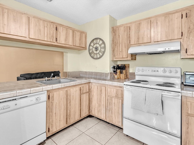 kitchen featuring white appliances, under cabinet range hood, a sink, light brown cabinetry, and a textured ceiling