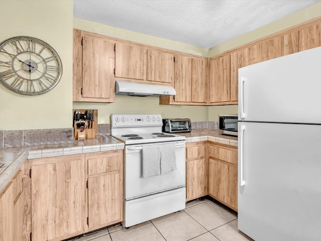 kitchen with white appliances, under cabinet range hood, light brown cabinets, tile countertops, and a textured ceiling