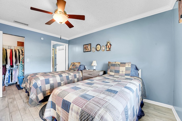 bedroom with light wood-style flooring, a textured ceiling, a closet, a ceiling fan, and a walk in closet