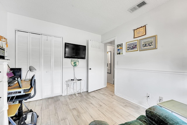 office space featuring light wood-style floors, a textured ceiling, and baseboards