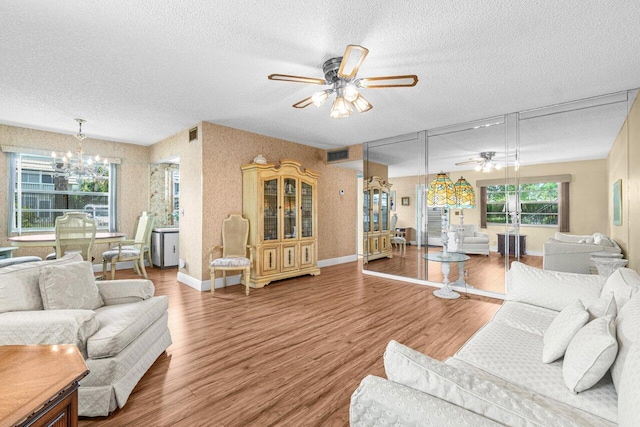 living area with a ceiling fan, a textured ceiling, a chandelier, wood finished floors, and baseboards