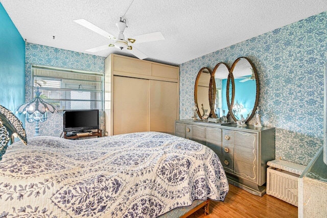 bedroom with wallpapered walls, wood finished floors, a closet, a textured ceiling, and ceiling fan