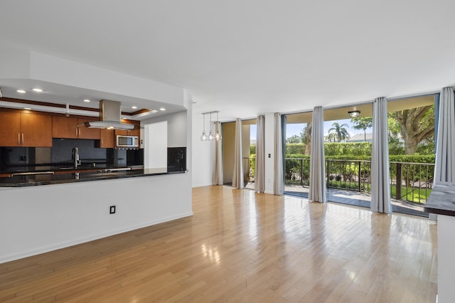unfurnished living room featuring healthy amount of natural light, a wall of windows, light wood-style floors, a sink, and recessed lighting