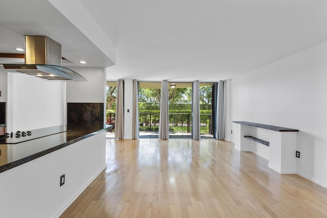 unfurnished living room with a wall of windows, baseboards, light wood-type flooring, and recessed lighting