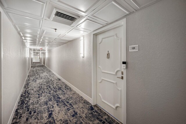 corridor with a textured wall, baseboards, coffered ceiling, and carpet flooring