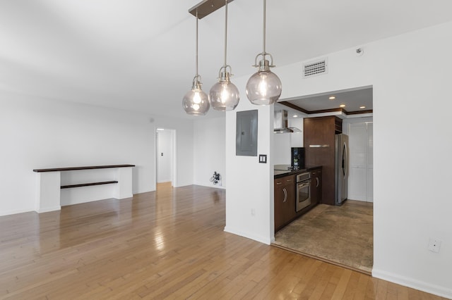 kitchen with appliances with stainless steel finishes, wall chimney exhaust hood, light wood finished floors, dark countertops, and electric panel