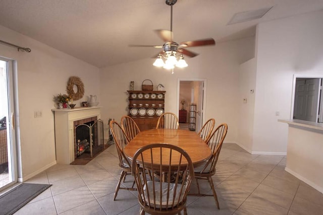 dining room featuring lofted ceiling, ceiling fan, a warm lit fireplace, light tile patterned floors, and baseboards
