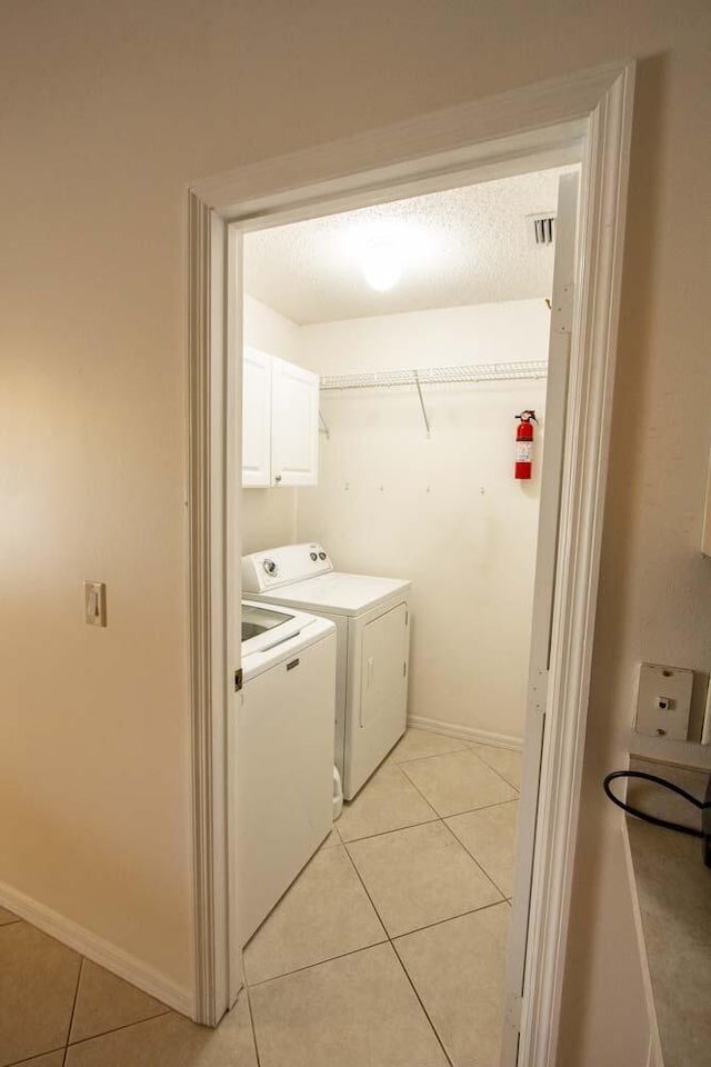 clothes washing area with light tile patterned floors, washer and clothes dryer, cabinet space, and baseboards