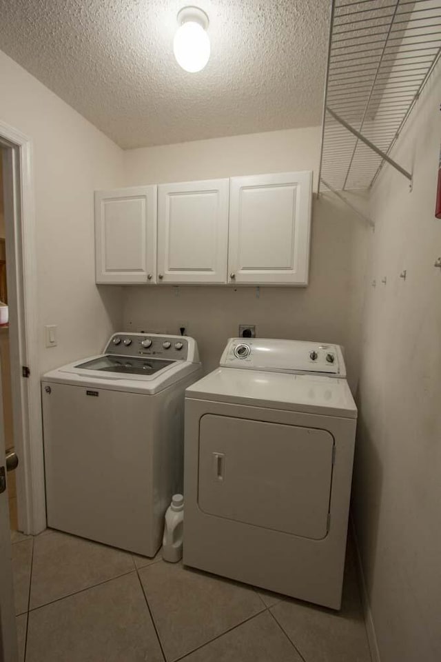 laundry area with cabinet space, separate washer and dryer, a textured ceiling, and light tile patterned floors