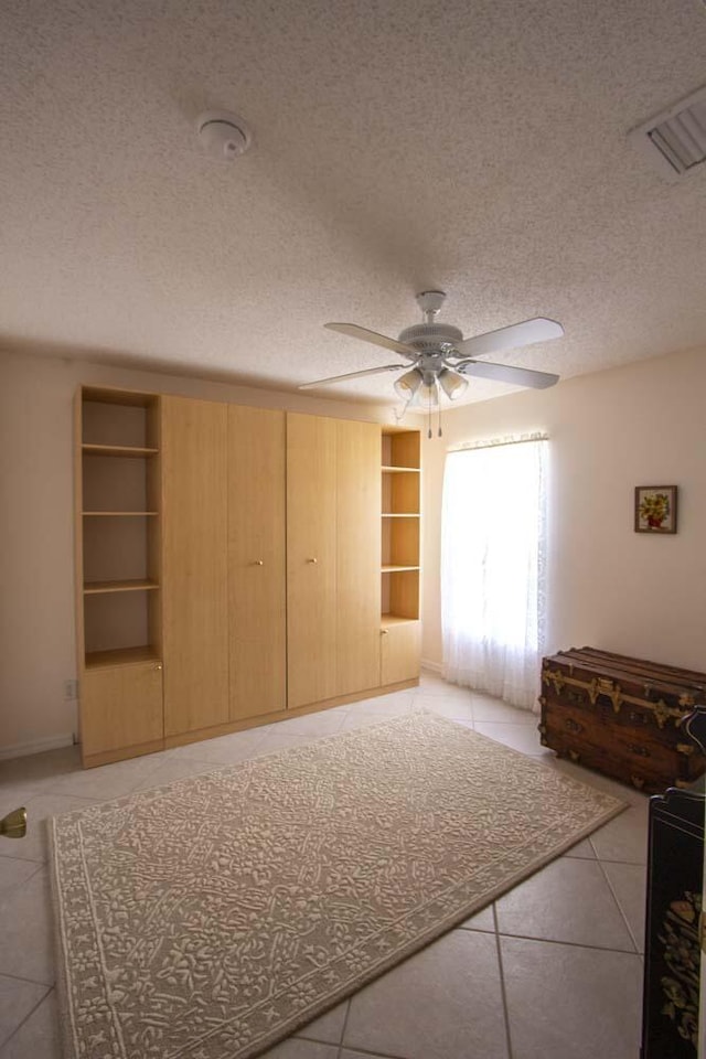 unfurnished living room with built in shelves, a ceiling fan, light tile patterned floors, and a textured ceiling