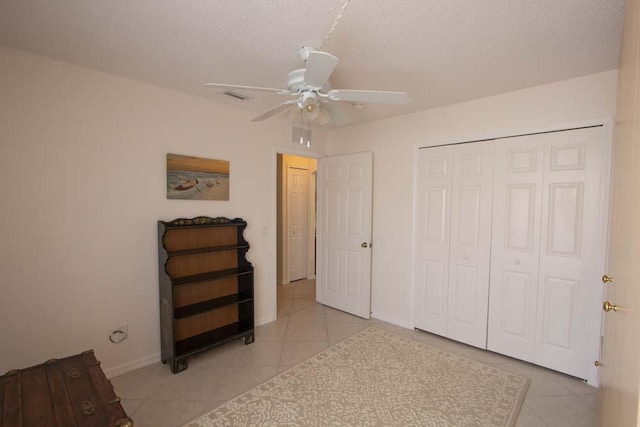 unfurnished bedroom with light tile patterned flooring, baseboards, a closet, ceiling fan, and a textured ceiling