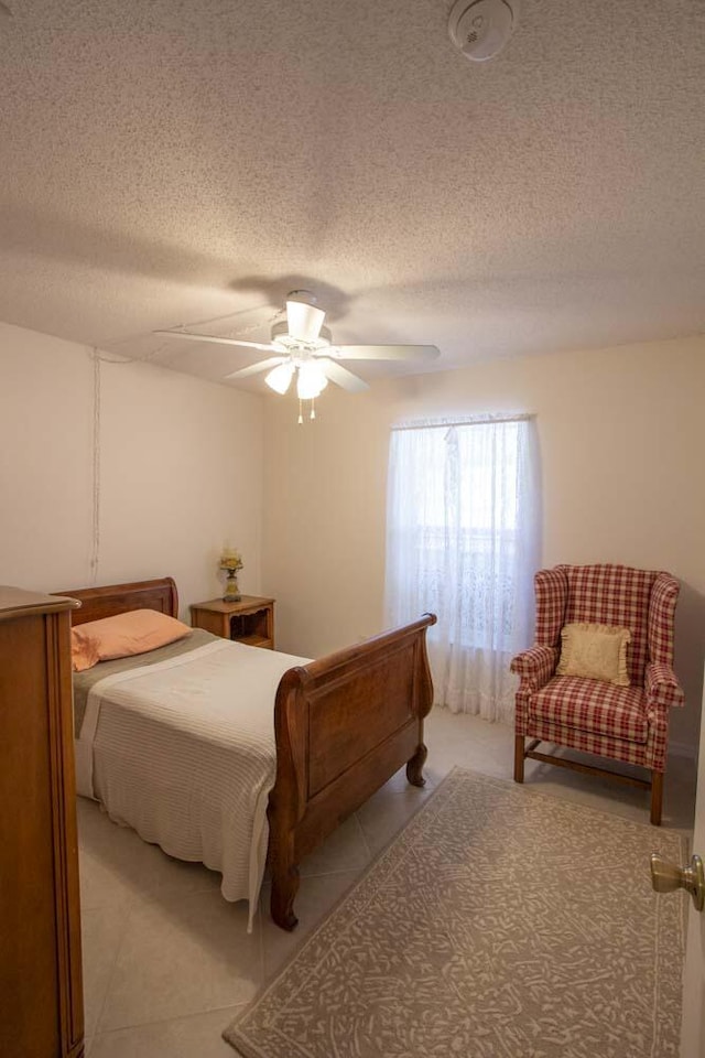 bedroom with a textured ceiling, light tile patterned floors, and ceiling fan