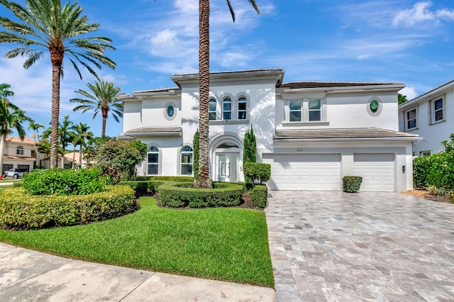 mediterranean / spanish-style house with a garage, stucco siding, a front yard, and decorative driveway