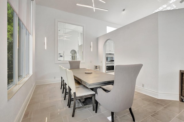 dining area featuring arched walkways, baseboards, and light tile patterned floors